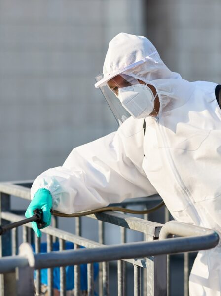 Healthcare worker in protective suit disinfecting outdoor public area.