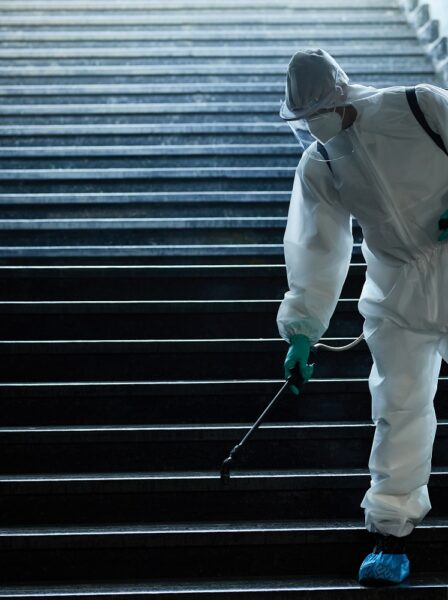 Man in protective suit disinfecting staircase of underground passage in order to prevent the spread of coronavirus.