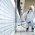 Unrecognizable worker in chemical protection suit spraying disinfectant on public surfaces. Person in white chemical protection suit doing disinfection of public areas to stop spreading highly contagious corona virus.