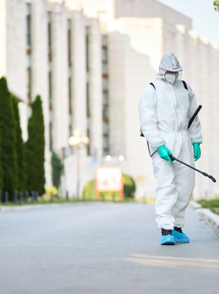 Disinfectant worker in protective suit sanitizing empty city streets during COVID-19 epidemic.